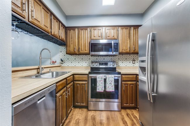 Kitchen with appliances with stainless steel finishes, light wood finished floors, tasteful backsplash, and brown cabinetry | Image 9