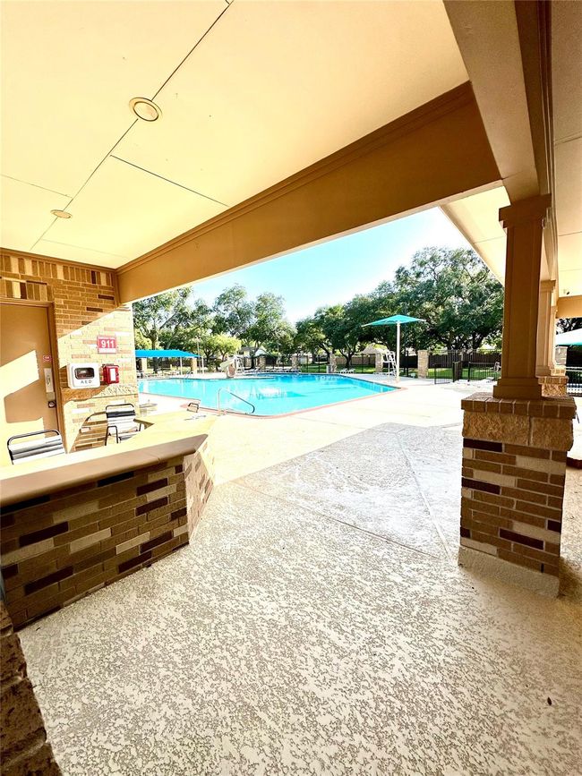 This photo showcases a community pool area with a shaded seating section, surrounded by trees. It offers a clean, inviting space perfect for relaxation and recreation. | Image 16