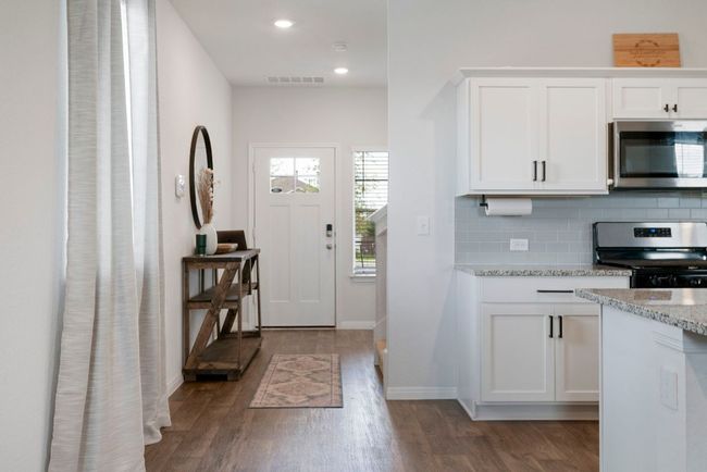 Kitchen with stainless steel appliances, dark wood finished floors, tasteful backsplash, white cabinetry, and light stone countertops | Image 10