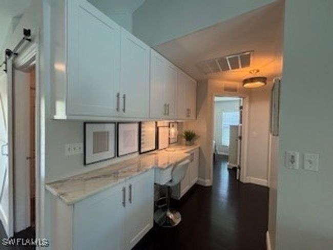 Kitchen with light stone counters, white cabinets, dark wood finished floors, visible vents, and built in desk | Image 13