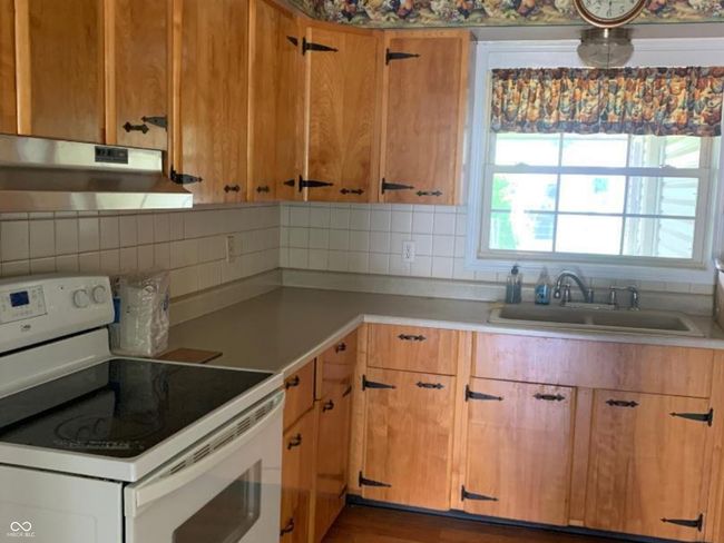 kitchen featuring white electric range, under cabinet range hood, wood finished floors, and tasteful backsplash | Image 4