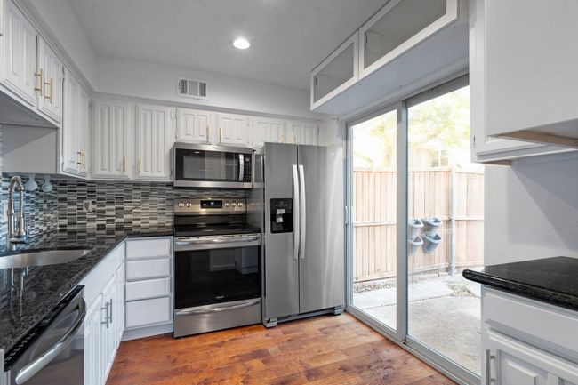 Kitchen with backsplash, visible vents, stainless steel appliances, a sink, and wood finished floors | Image 12