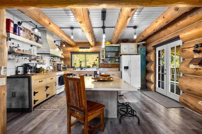 Kitchen with open shelves, white appliances, rustic walls, dark wood finished floors, and custom range hood | Image 16