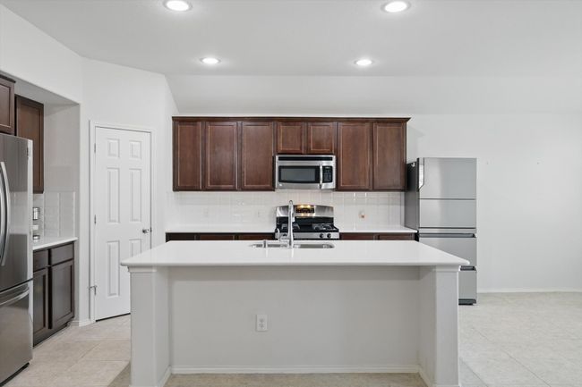 Kitchen featuring dark brown cabinets, a sink, stainless steel appliances, light countertops, and backsplash | Image 23