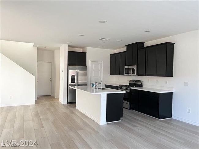 Kitchen with a sink, light countertops, appliances with stainless steel finishes, dark cabinetry, and light wood-style flooring | Image 6