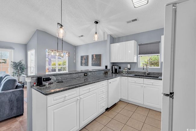 Kitchen featuring white appliances, a peninsula, healthy amount of natural light, white cabinets, and lofted ceiling | Image 21