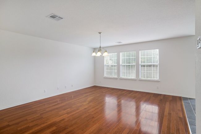 Empty room with an inviting chandelier, baseboards, dark wood-style flooring, and visible vents | Image 8