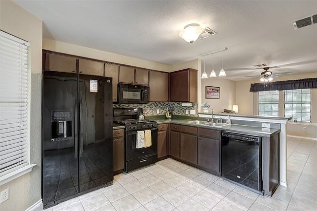 Kitchen with black appliances, a sink, a peninsula, and light tile patterned floors | Image 15