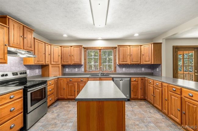 Kitchen featuring a textured ceiling, backsplash, stainless steel appliances, a kitchen island, and sink | Image 38