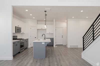 Kitchen featuring appliances with stainless steel finishes, a kitchen island with sink, hanging light fixtures, sink, and white cabinetry | Image 2