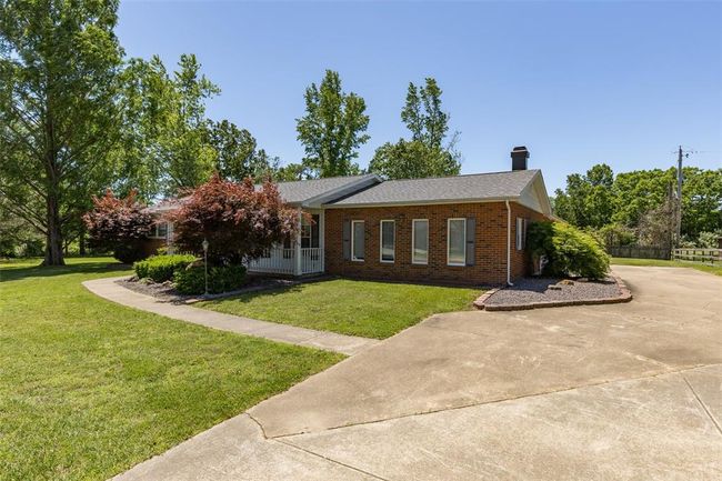 Ranch-style home with brick siding, a chimney, concrete driveway, and roof with shingles | Image 4