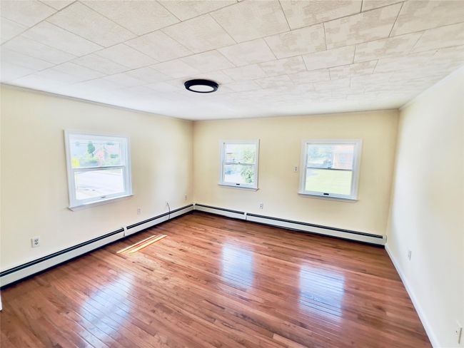Unfurnished room featuring hardwood / wood-style floors and a baseboard heating unit | Image 8