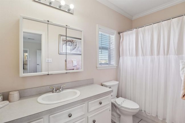The primary bathroom offers a clean and airy design with a tub/shower combination, perfect for versatility and relaxation. A large mirrored medicine cabinet and extended vanity provide ample storage and counter space. Soft neutral tones, a bright window, and finishes create a calming atmosphere, complementing the primary suite's serene aesthetic. | Image 15