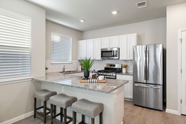 Kitchen featuring light stone countertops, a kitchen breakfast bar, white cabinetry, and stainless steel appliances | Image 10