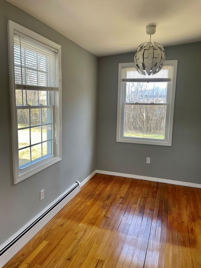 Unfurnished room featuring a notable chandelier, plenty of natural light, a baseboard heating unit, and hardwood / wood-style flooring | Image 9