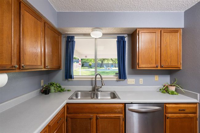 Kitchen featuring brown cabinetry, a textured ceiling, dishwasher, light countertops, and a sink | Image 10