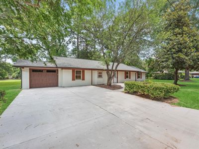 This is a single-story home featuring a large front yard with mature trees, a spacious driveway, and an attached garage. The house has a traditional design with a welcoming exterior. | Image 3