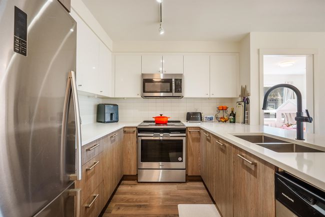 Kitchen featuring stainless steel appliances, dark wood-style floors, light countertops, and decorative backsplash | Image 8