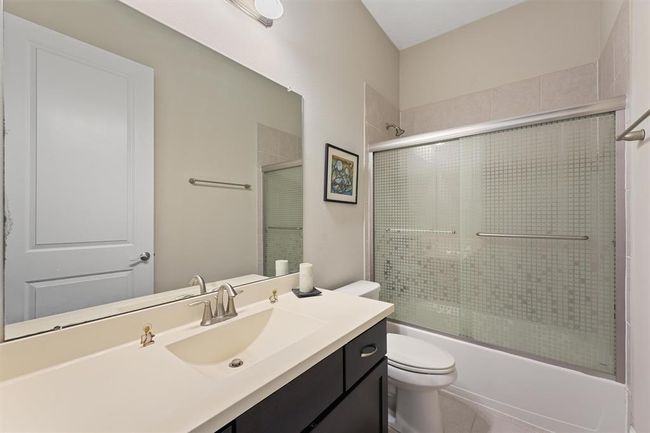 Private ensuite bathroom for the downstairs secondary bedroom, featuring a sleek vanity with modern fixtures, a tub/shower combo with sliding glass doors, and neutral tile finishes. A perfect setup for guests or multigenerational living. | Image 16