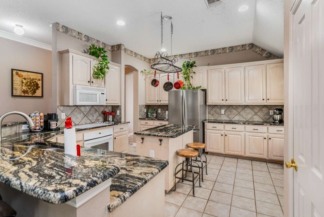 Kitchen featuring appliances, a breakfast bar, a peninsula, backsplash, and marble counter tops. | Image 16