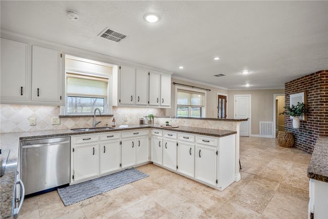 Kitchen featuring visible vents, white cabinets, a peninsula, stainless steel dishwasher, and a sink | Image 16