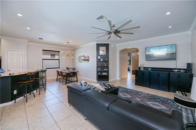 Living room featuring visible vents, ornamental molding, arched walkways, ceiling fan with notable chandelier, and light tile patterned floors | Image 6