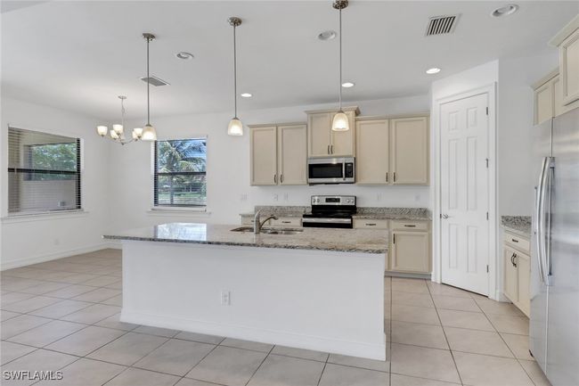 Kitchen with appliances with stainless steel finishes, a sink, light stone countertops, a chandelier, and light tile patterned floors | Image 26