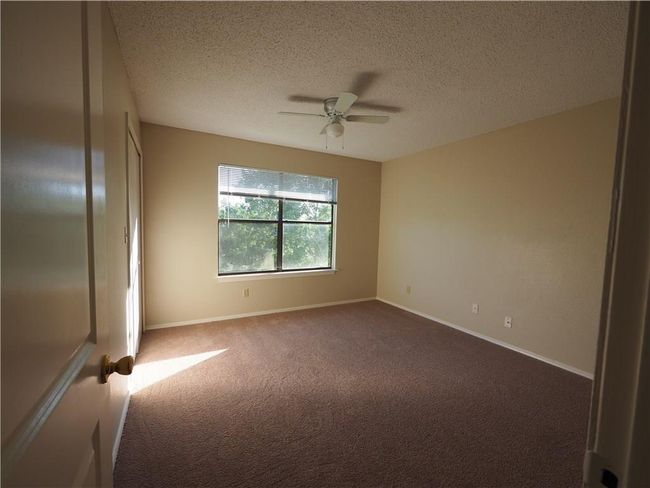 Empty room featuring dark carpet, ceiling fan, a textured ceiling, and baseboards | Image 13
