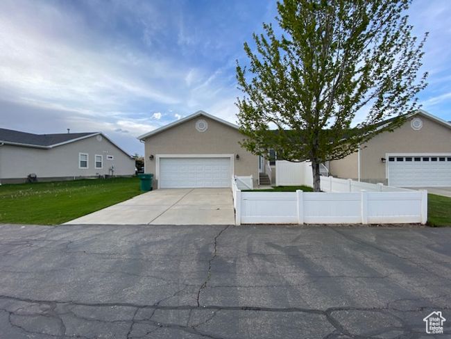 View of back of house featuring concrete driveway, stucco siding, a fenced front yard, a front yard, and a garage | Image 21
