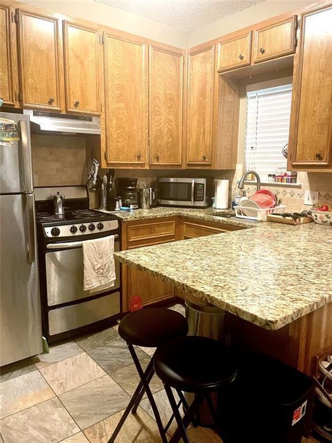 Kitchen featuring appliances with stainless steel finishes, under cabinet range hood, a breakfast bar, a peninsula, and light stone countertops | Image 15