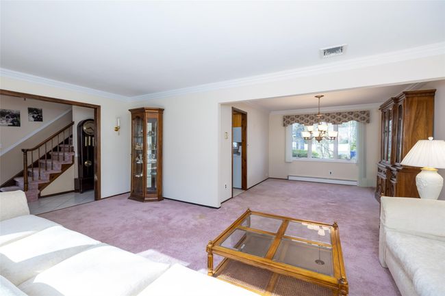 Living room with a baseboard radiator, ornamental molding, light carpet, visible vents, and a notable chandelier | Image 13