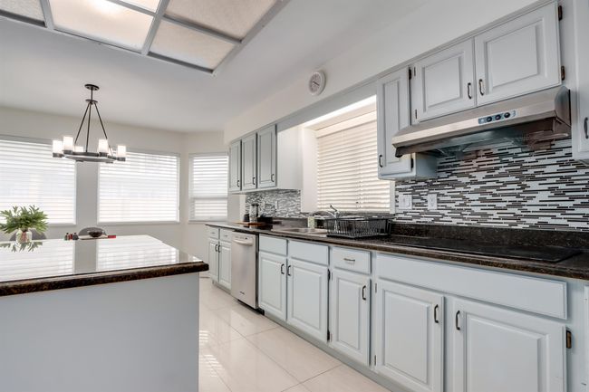 Kitchen with under cabinet range hood, black electric cooktop, tasteful backsplash, decorative light fixtures, and a chandelier | Image 8