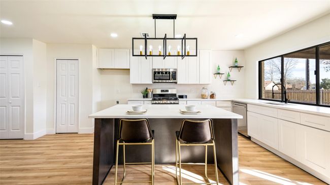 Kitchen featuring light wood-style flooring, a center island, white cabinets, stainless steel appliances, and a sink | Image 9