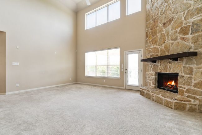 Unfurnished living room featuring a high ceiling, carpet, a fireplace, and plenty of natural light | Image 7