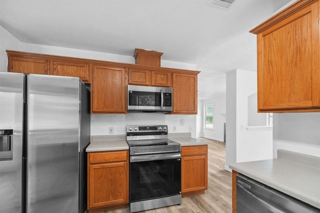 Kitchen with visible vents, brown cabinetry, light wood-style floors, light countertops, and stainless steel appliances | Image 15