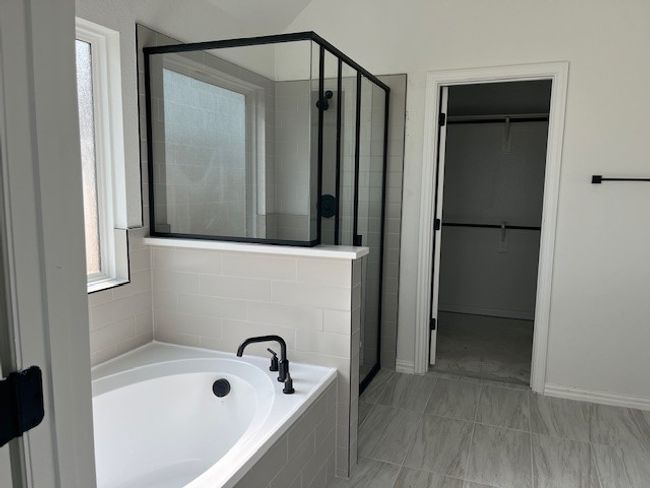 Bathroom with a stall shower, a walk in closet, a garden tub, and baseboards | Image 5