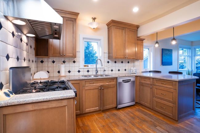Kitchen with stainless steel dishwasher, dark wood finished floors, a sink, a peninsula, and ventilation hood | Image 8