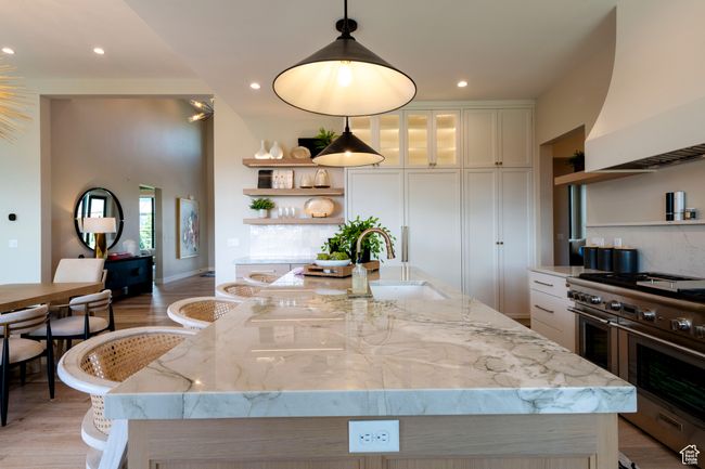 Kitchen featuring range with two ovens, premium range hood, open shelves, white cabinets, and a center island with sink | Image 18