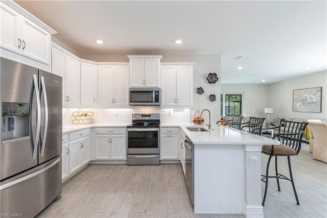 Kitchen featuring stainless steel appliances, a peninsula, a sink, light countertops, and a kitchen bar | Image 8