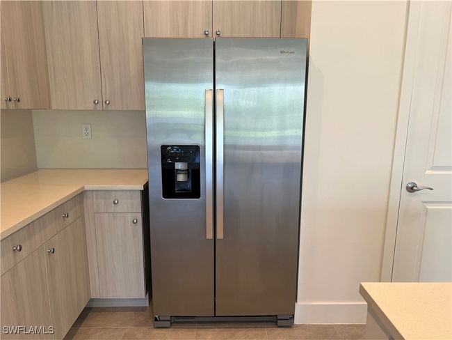 Kitchen with light tile patterned floors, light brown cabinets, and stainless steel fridge with ice dispenser | Image 12