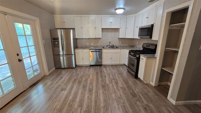 Kitchen featuring stainless steel appliances, wood finished floors, white cabinets, and light stone countertops | Image 5