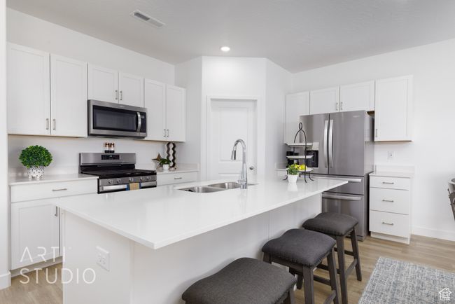 Kitchen featuring a breakfast bar area, a sink, visible vents, stainless steel appliances, and light wood-type flooring | Image 12