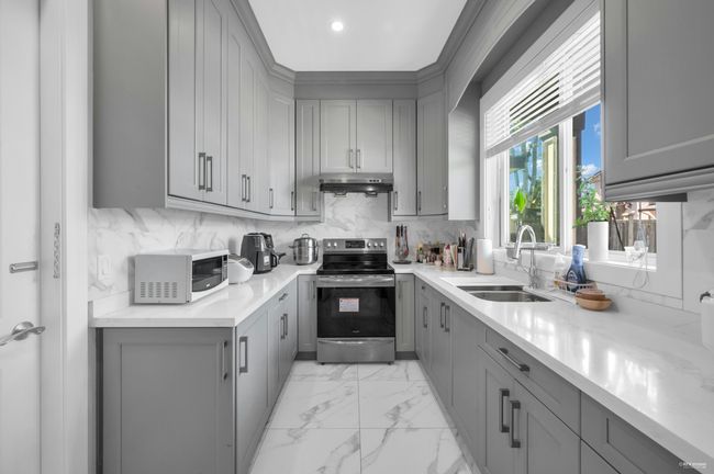 Kitchen with gray cabinets, stainless steel electric stove, white microwave, under cabinet range hood, and backsplash | Image 14
