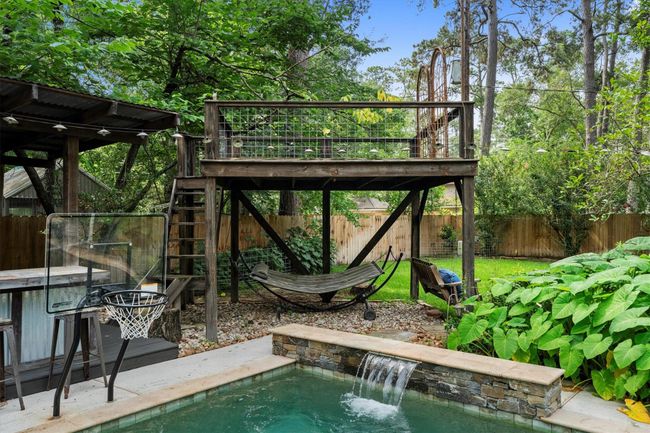 This backyard features a serene and lush setting with a wooden deck, hammock, and a pool with a waterfall. | Image 41