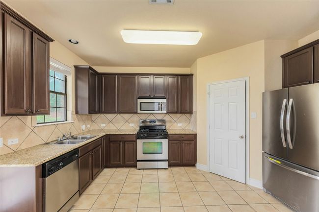Kitchen featuring appliances with stainless steel finishes, dark brown cabinets, decorative backsplash, and light tile patterned floors | Image 9