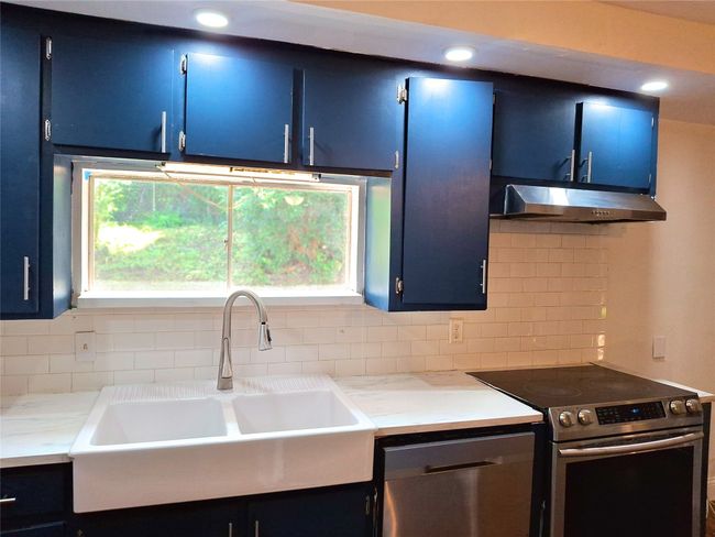 Kitchen with blue cabinetry, appliances with stainless steel finishes, under cabinet range hood, a sink, and backsplash | Image 6