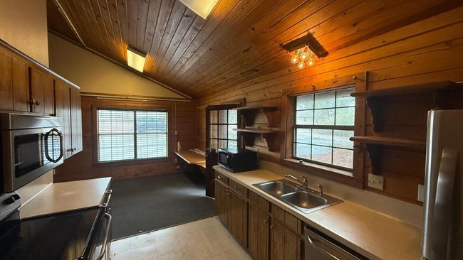Kitchen featuring open shelves, a sink, appliances with stainless steel finishes, wooden walls, and vaulted ceiling | Image 20