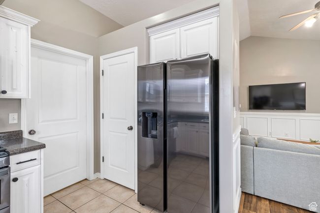 Kitchen featuring vaulted ceiling, white cabinets, stainless steel fridge, light tile patterned floors, and ceiling fan | Image 4