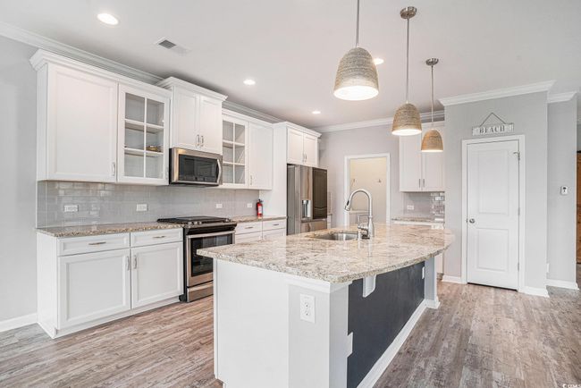 Kitchen with appliances with stainless steel finishes, ornamental molding, light wood-style floors, tasteful backsplash, and white cabinetry | Image 5