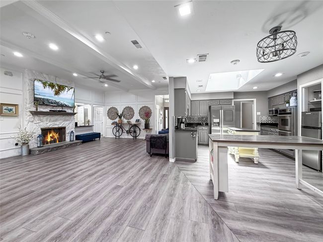 Living room with a ceiling fan, light wood-style flooring, a stone fireplace, beamed ceiling, and a decorative wall | Image 12